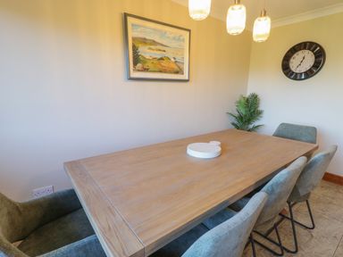 A dining room with a wooden table six chairs a wall clock a painting and a plant at Nelly's House in Gortahork County Donegal