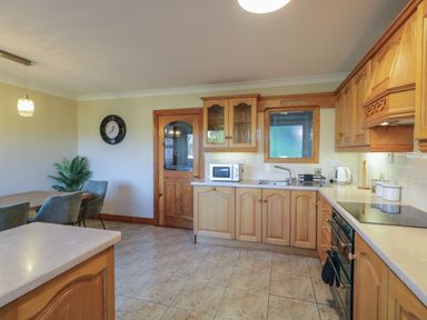 A kitchen with wooden cabinets a dining table with chairs a clock on the wall and kitchen appliances at Nelly's House in Gortahork County Donegal