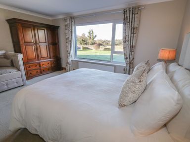 A bedroom with a large bed and pillows a wooden wardrobe a window with curtains and a lamp at Nelly's House in Gortahork County Donegal
