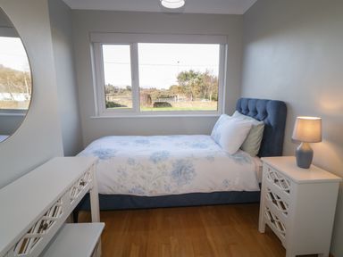 A bedroom with a single bed with floral bedding a side table with a lamp and a vanity table near a window at Nelly's House in Gortahork County Donegal