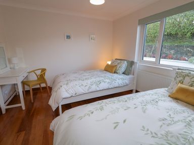 A bedroom with two single beds a desk with a chair and a window showing plants outside at Nelly's House in Gortahork County Donegal