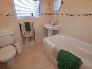 A bathroom with a toilet a pedestal sink a bathtub with towels and a window with blinds at Nelly's House in Gortahork County Donegal