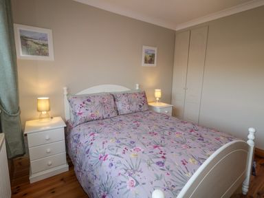 A bedroom with a bed with floral bedding two bedside tables with lamps and two framed pictures on the wall at Nelly's House in Gortahork County Donegal