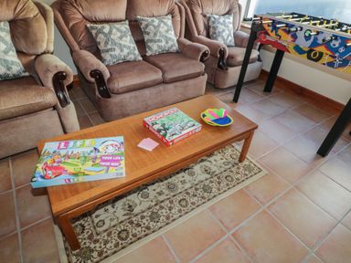 A room with three brown upholstered armchairs a wooden coffee table with board games and paddle ball set and a foosball table at Nelly's House in Gortahork County Donegal