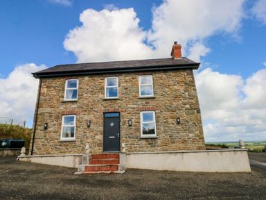 Stone house with four windows and a black door with steps on a paved area at Little Pale Near Whitland