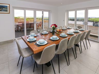 A dining room with a wooden table set for twelve people with bowls plates cutlery and glasses near large sliding glass doors at Little Pale Near Whitland