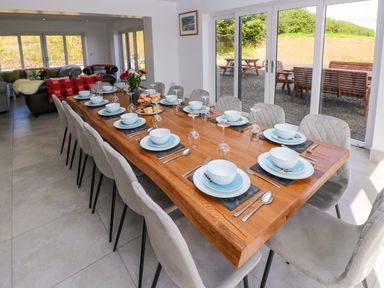 A dining room with a long wooden table set with plates bowls glasses and cutlery and chairs around it at Little Pale Near Whitland