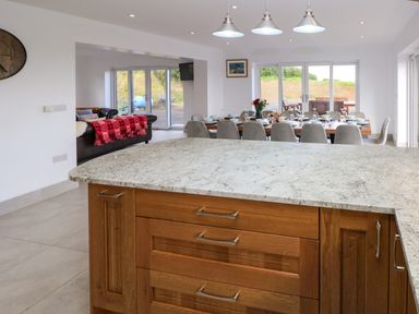A kitchen island with wooden cabinets in front of a dining table with chairs and tableware at Little Pale Near Whitland