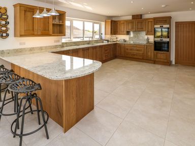 A kitchen with wooden cabinets a granite countertop bar stools and tiled floor at Little Pale Near Whitland