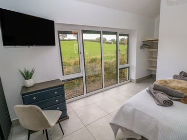 A bedroom with a bed towels closet and a dresser with a chair near large glass windows at Little Pale Near Whitland