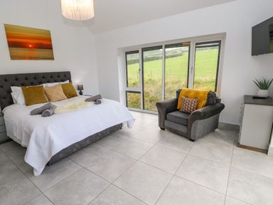 A bedroom with a bed beside a window and an armchair at Little Pale Near Whitland