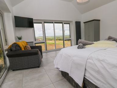 A bedroom with a bed, armchair, TV, wardrobe, and large windows overlooking a landscape at Little Pale Near Whitland