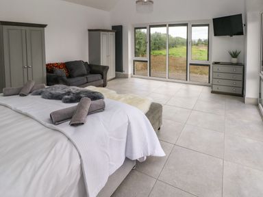 A bedroom with a bed towels sofa cabinets and a wall mounted tv near large windows at Little Pale Near Whitland