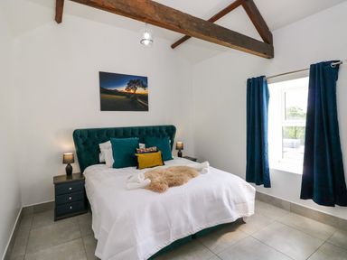 A bedroom with a bed with teal headboard and pillows two bedside tables with lamps and a window with blue curtains at Little Pale Near Whitland