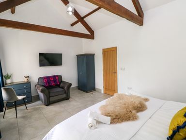 A bedroom with a bed a gray armchair a blue dresser a blue wardrobe a wooden door and exposed wooden ceiling beams at Little Pale Near Whitland