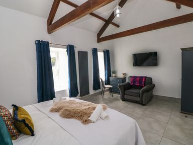 A bedroom with a bed a chair a dresser a wall-mounted television and wooden ceiling beams at Little Pale Near Whitland