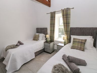 A bedroom with two single beds plaid cushions bedside tables with lamps and a window with plaid curtains at Little Pale Near Whitland