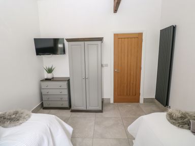 A bedroom with two twin beds a wooden door a grey wardrobe a dresser with a plant and a mounted TV at Little Pale Near Whitland