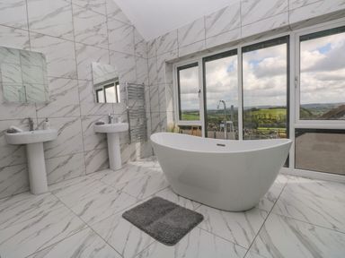 A bathroom with two pedestal sinks mirrors and a freestanding bathtub near windows showing countryside at Little Pale Near Whitland