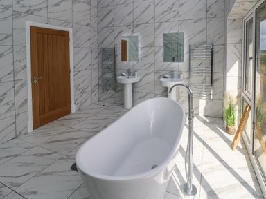 A bathroom with a freestanding bathtub two pedestal sinks mirrors towel rails and a wooden door at Little Pale Near Whitland