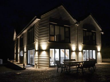 An illuminated two-story house with outdoor wooden table and benches at Little Pale Near Whitland
