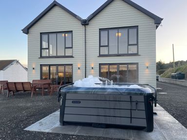A hot tub with bubbles in front of a two-story house with outdoor wooden benches and tables at Little Pale Near Whitland