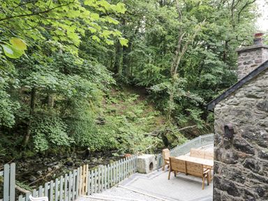 An outdoor area with a table and chairs near a stream at Frongoch Old Power House in Dolgellau