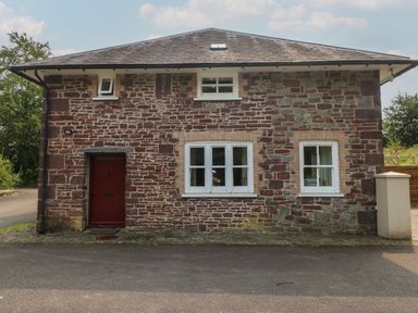 Exterior of a two-story stone house with white framed windows and a red door at Clearbrook Lodge in Llanarthney nr Llandeilo Carmarthenshire
