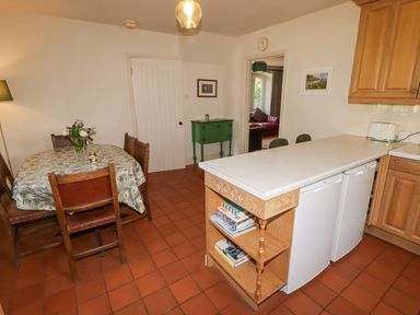 A kitchen with a dining table with flowers a kitchen island with books and two white appliances at Clearbrook Lodge in Llanarthney nr Llandeilo Carmarthenshire