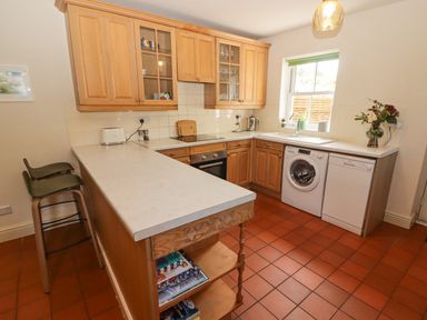 A kitchen with wooden cabinets a white countertop a washing machine dishwasher two bar stools and a window at Clearbrook Lodge in Llanarthney nr Llandeilo Carmarthenshire