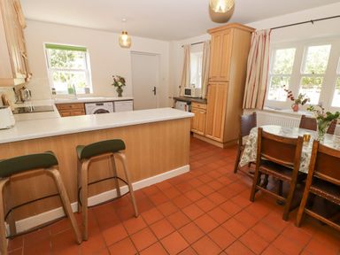 A kitchen with wooden cabinets a countertop with two stools a dining table with chairs and windows at Clearbrook Lodge Llanarthney nr Llandeilo Carmarthenshire