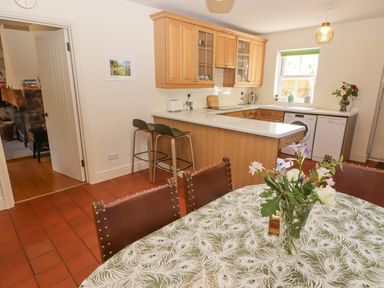 A kitchen with wooden cabinets bar stools and a table with a floral tablecloth and flowers at Clearbrook Lodge in Llanarthney nr Llandeilo Carmarthenshire