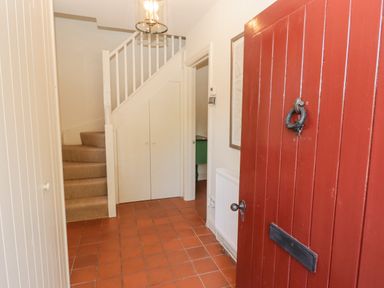 An entrance hallway with a red door tiled floor stairs with beige carpet and white banister under stairs storage at Clearbrook Lodge Llanarthney nr Llandeilo Carmarthenshire