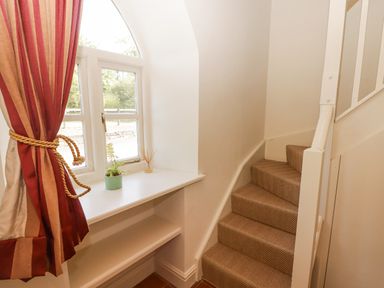 A staircase with carpeted steps next to a window with red and beige curtains and a small shelf with a plant at Clearbrook Lodge in Llanarthney nr Llandeilo Carmarthenshire