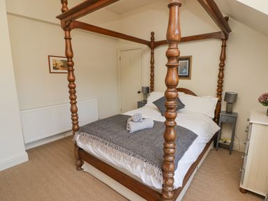 A bedroom with a wooden four-poster bed a gray blanket and rolled towels on the bed bedside tables with lamps paintings on the walls and a chest of drawers with flowers at Clearbrook Lodge in Llanarthney nr Llandeilo Carmarthenshire