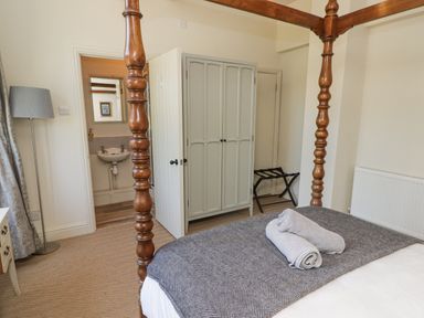 A bedroom with a wooden four poster bed a gray blanket towels on the bed a gray wardrobe an open door showing a sink a floor lamp and a luggage rack at Clearbrook Lodge Llanarthney nr Llandeilo Carmarthenshire