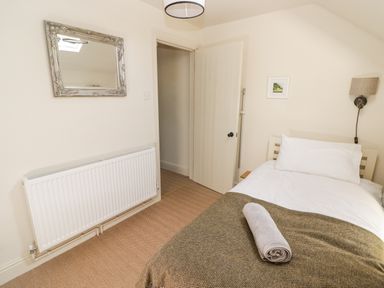 A bedroom with a single bed a rolled towel on the blanket a wall mirror radiator and an open door at Clearbrook Lodge Llanarthney nr Llandeilo Carmarthenshire