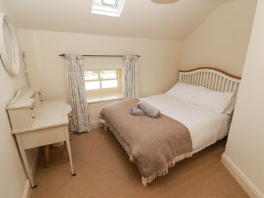 A bedroom with a double bed a blanket and towels on top a desk with drawers a round mirror and a window with curtains at Clearbrook Lodge Llanarthney nr Llandeilo Carmarthenshire