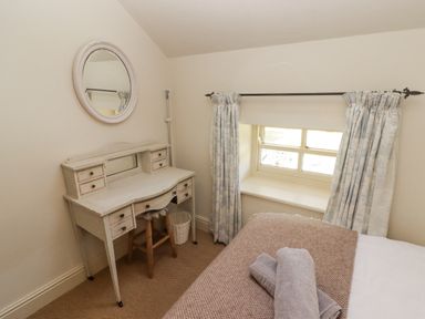 A bedroom corner with a window, curtains, a wooden dressing table, a stool, and a bed with folded towels at Clearbrook Lodge in Llanarthney, nr Llandeilo, Carmarthenshire