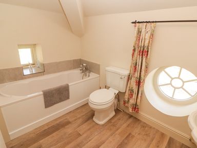 A bathroom with a bathtub a toilet a circular window and floral curtains at Clearbrook Lodge in Llanarthney nr Llandeilo Carmarthenshire