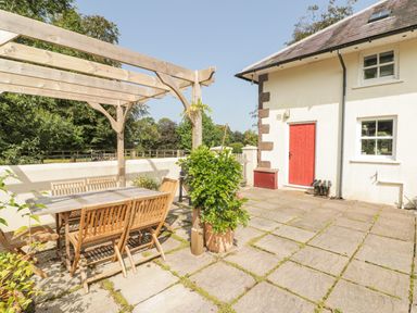 An outdoor patio with a wooden pergola and dining table with chairs near a white building with a red door at Clearbrook Lodge Llanarthney nr Llandeilo Carmarthenshire
