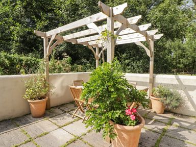 A wooden pergola with a table and chairs on a stone patio with potted plants at Clearbrook Lodge in Llanarthney nr Llandeilo Carmarthenshire