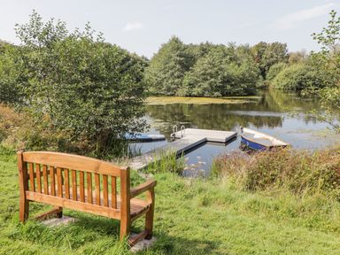 A wooden bench facing a small dock on a lake with a blue rowboat and paddleboard surrounded by trees at Clearbrook Lodge in Llanarthney nr Llandeilo Carmarthenshire
