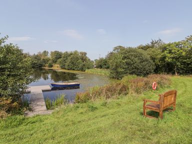 A small wooden bench near a dock with a boat on a pond surrounded by grass and trees at Clearbrook Lodge in Llanarthney nr Llandeilo Carmarthenshire