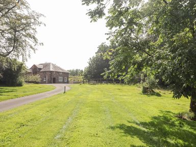 A stone house at the end of a driveway with a large lawn and trees around it at Clearbrook Lodge in Llanarthney nr Llandeilo Carmarthenshire