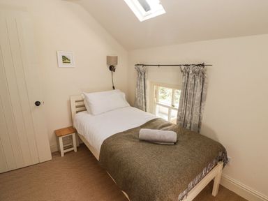 A bedroom with a single bed white bedding and a brown throw with a rolled towel on top at Clearbrook Lodge in Llanarthney nr Llandeilo Carmarthenshire
