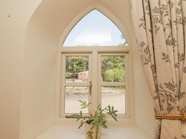 A window with a pointed arch design with a small plant on the sill and patterned curtains at Clearbrook Lodge in Llanarthney nr Llandeilo Carmarthenshire