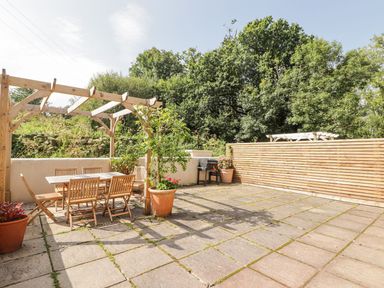 An outdoor patio area with wooden table and chairs under a pergola and potted plants at Clearbrook Lodge in Llanarthney nr Llandeilo Carmarthenshire