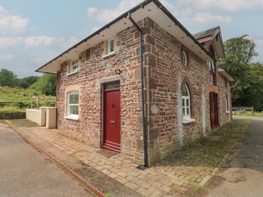 A stone brick house with red doors and windows next to a paved path at Clearbrook Lodge in Llanarthney nr Llandeilo Carmarthenshire