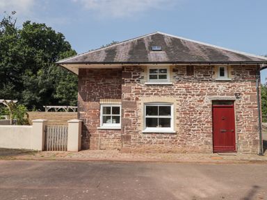 A stone cottage with white framed windows and a red door with a wooden gate and trees behind Meadow Cottage Llanarthney nr Llandeilo Carmarthenshire